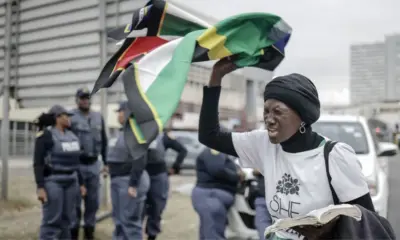 Mulher sul-africana protesta com a bandeira da África do Sul enquanto policiais acompanham manifestação durante tensão causada por ultimato de grupos anti-imigração.